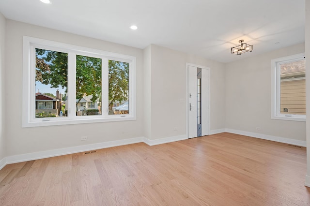 unfurnished room featuring a notable chandelier, plenty of natural light, and light wood-type flooring