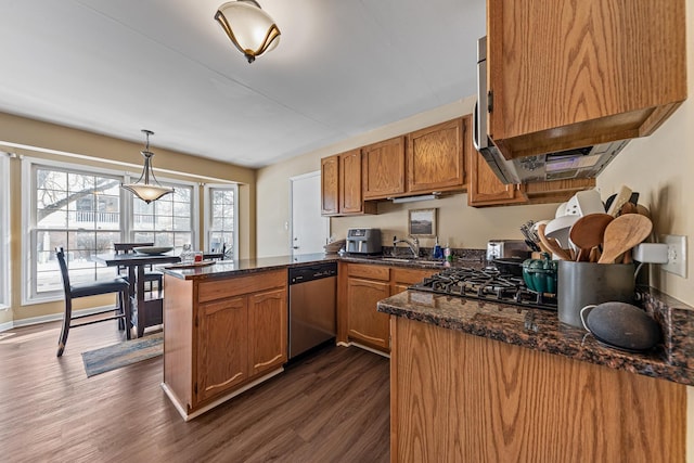 kitchen with pendant lighting, dark wood-type flooring, stainless steel dishwasher, dark stone countertops, and kitchen peninsula