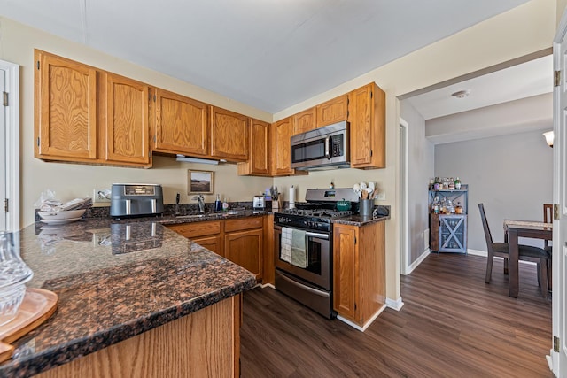 kitchen with sink, dark hardwood / wood-style floors, dark stone countertops, kitchen peninsula, and stainless steel appliances