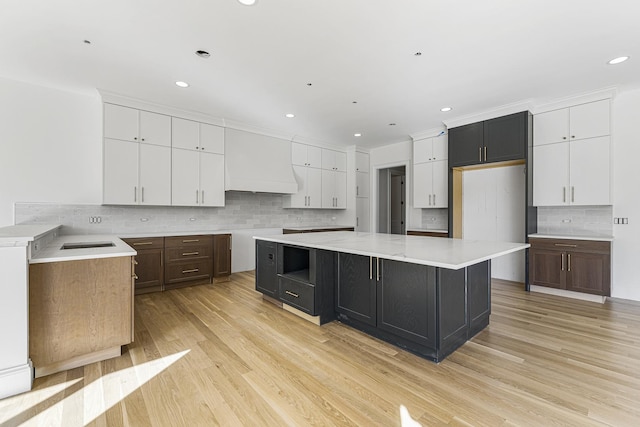 kitchen featuring custom range hood, light hardwood / wood-style floors, tasteful backsplash, and a large island