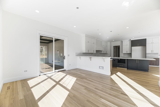 kitchen featuring a large island, light hardwood / wood-style floors, a kitchen bar, decorative backsplash, and custom exhaust hood