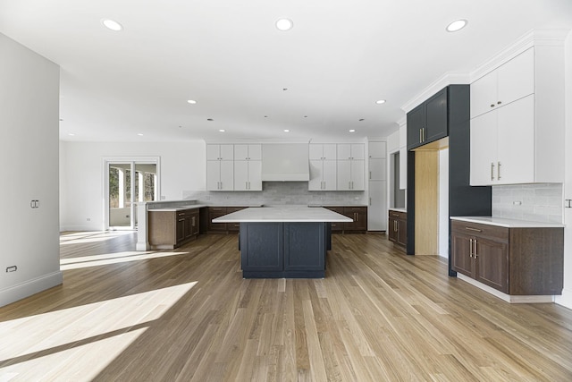 kitchen featuring tasteful backsplash, dark brown cabinets, light hardwood / wood-style flooring, white cabinets, and a center island