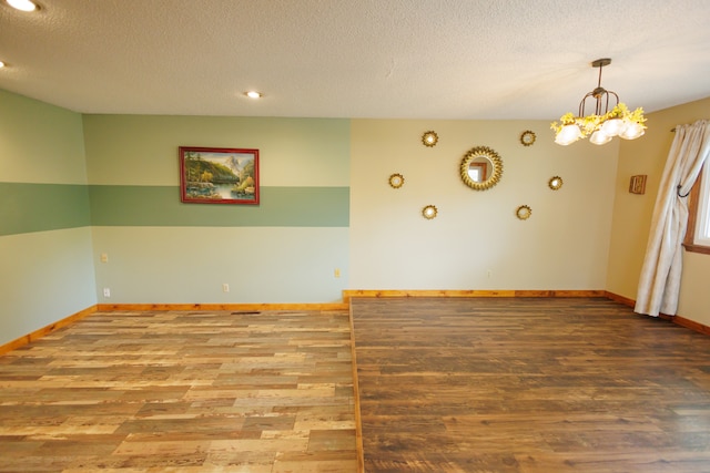 unfurnished room featuring hardwood / wood-style flooring, a textured ceiling, and an inviting chandelier