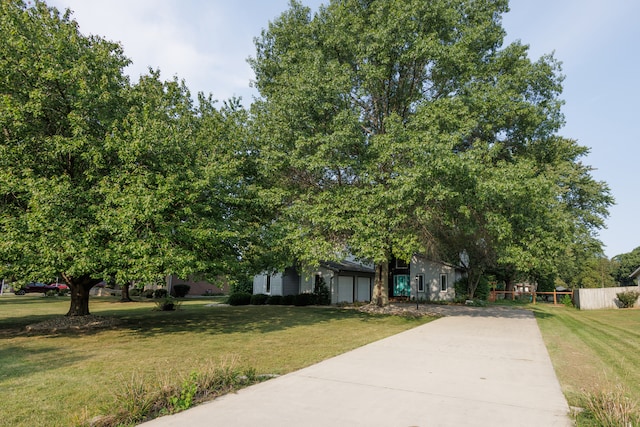 view of property hidden behind natural elements featuring a garage and a front lawn