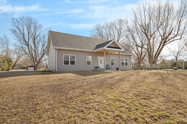 view of front facade with a shingled roof, a front yard, fence, and an outdoor structure