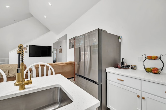 kitchen with freestanding refrigerator, open floor plan, white cabinets, vaulted ceiling, and a sink