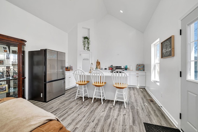 kitchen with light wood-style floors, white cabinetry, a kitchen breakfast bar, and freestanding refrigerator