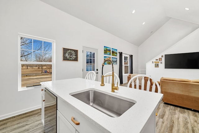 kitchen with dishwasher, light stone counters, vaulted ceiling, light wood-type flooring, and a sink