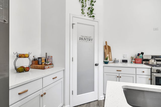 kitchen featuring light stone countertops, stainless steel gas range oven, white cabinetry, and wood finished floors