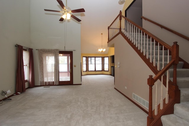 unfurnished living room with a high ceiling, ceiling fan with notable chandelier, and light colored carpet