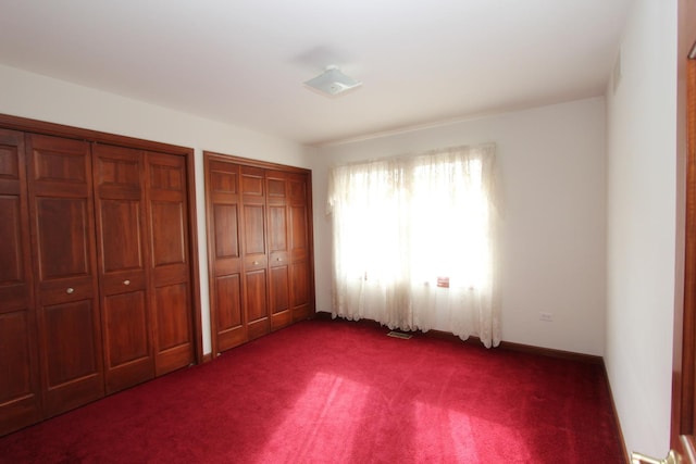 unfurnished bedroom with multiple closets and dark colored carpet