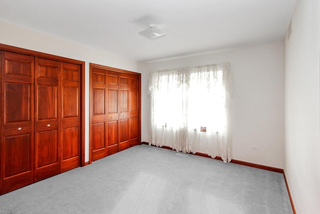 unfurnished bedroom featuring multiple closets and light carpet