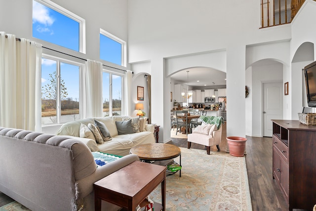 living room with a chandelier, a towering ceiling, and dark wood-type flooring