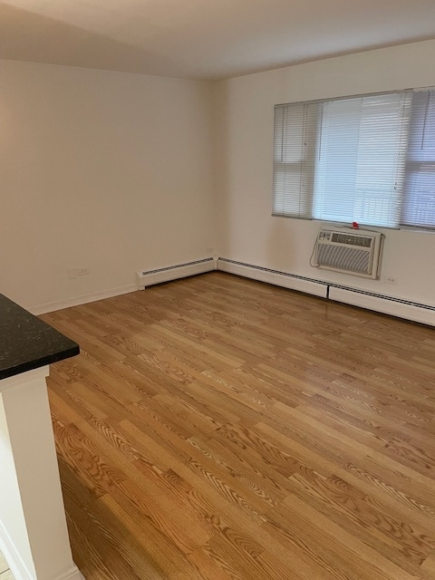 interior space featuring a wall mounted air conditioner, light wood-type flooring, and a baseboard radiator