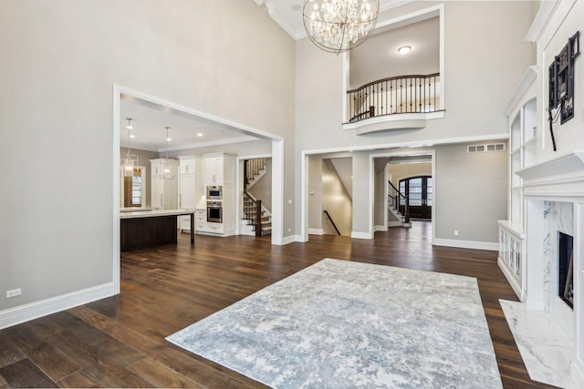 foyer featuring an inviting chandelier, a premium fireplace, dark wood-type flooring, a towering ceiling, and crown molding