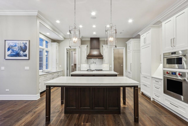 kitchen featuring white cabinetry, premium range hood, sink, hanging light fixtures, and a center island with sink