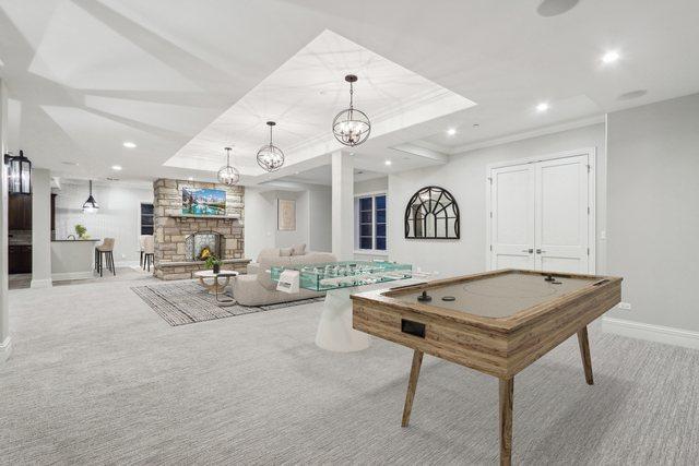 rec room with light colored carpet, a raised ceiling, and a stone fireplace