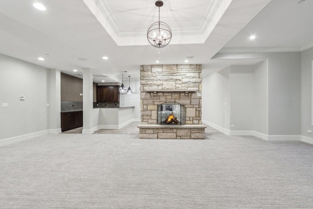 unfurnished living room featuring light carpet, a stone fireplace, ornamental molding, a notable chandelier, and a tray ceiling