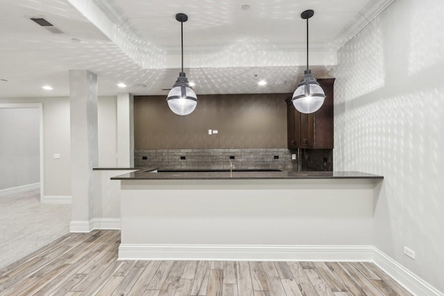 kitchen featuring pendant lighting, kitchen peninsula, crown molding, light hardwood / wood-style flooring, and dark brown cabinets