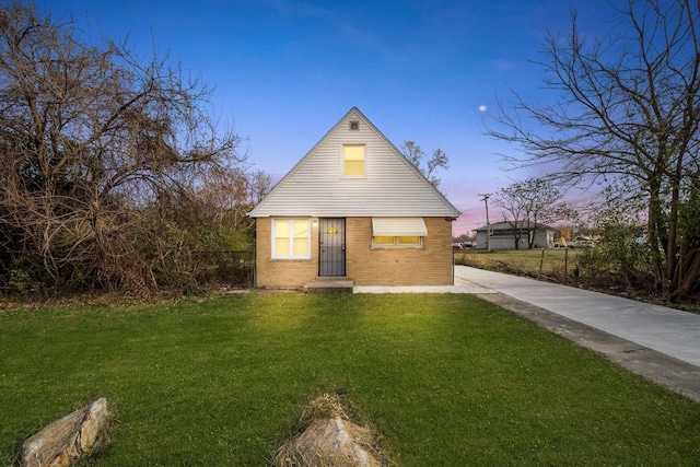 back of house at dusk with driveway, a yard, and brick siding