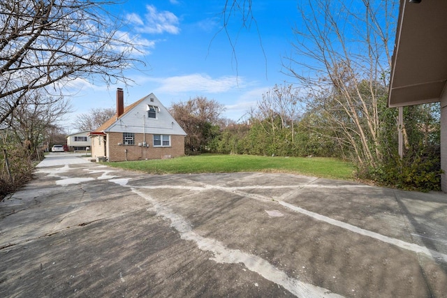 view of side of property featuring driveway, a yard, a chimney, and brick siding