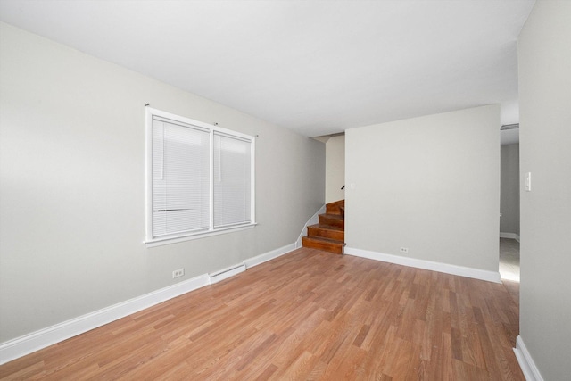 empty room featuring light wood-style flooring, stairway, baseboard heating, and baseboards