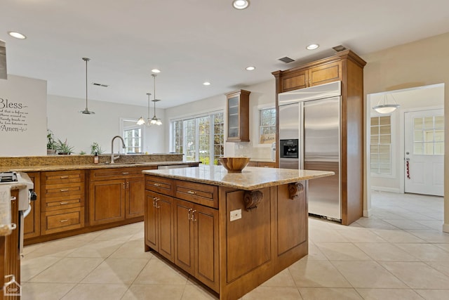 kitchen featuring sink, light tile patterned floors, built in fridge, decorative light fixtures, and a kitchen island