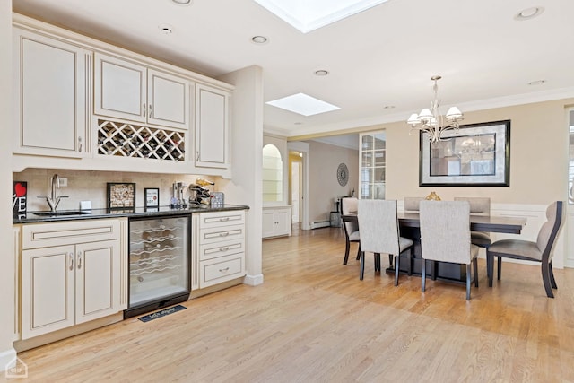 kitchen featuring sink, wine cooler, light hardwood / wood-style flooring, decorative light fixtures, and ornamental molding