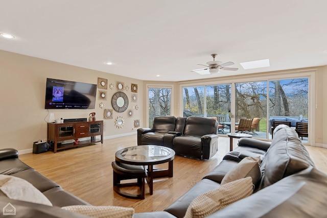 living room featuring a skylight, ceiling fan, and light hardwood / wood-style floors