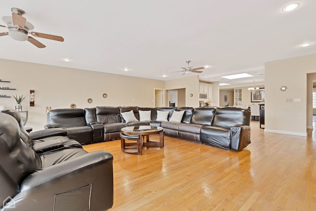 living room with ceiling fan with notable chandelier, light wood-type flooring, and a skylight