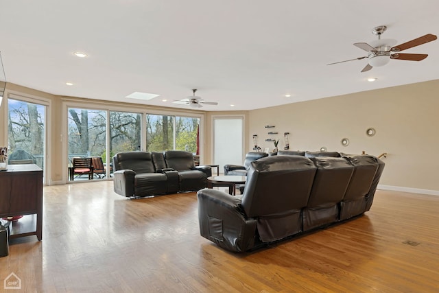 living room featuring a skylight, light hardwood / wood-style flooring, and ceiling fan