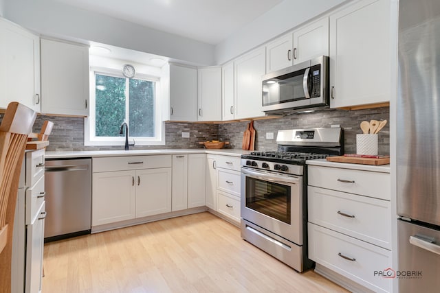 kitchen featuring decorative backsplash, light wood-type flooring, stainless steel appliances, sink, and white cabinetry