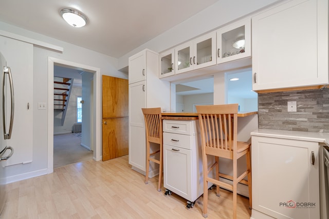 kitchen with light wood-type flooring, white cabinetry, and tasteful backsplash