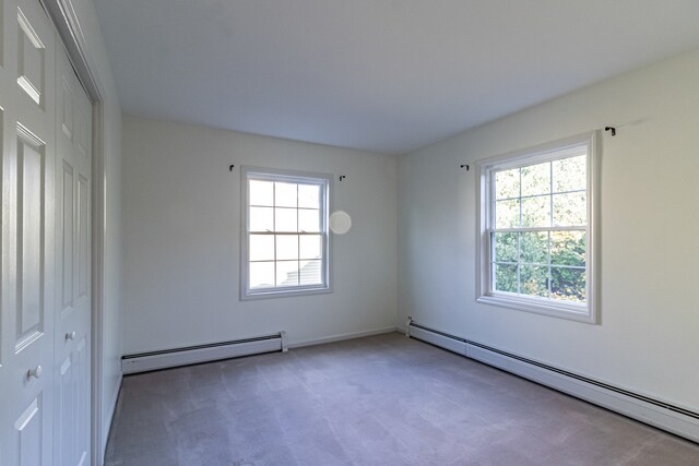 carpeted spare room with a baseboard heating unit