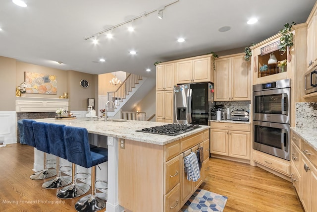 kitchen with light brown cabinetry, a breakfast bar, rail lighting, appliances with stainless steel finishes, and light stone countertops