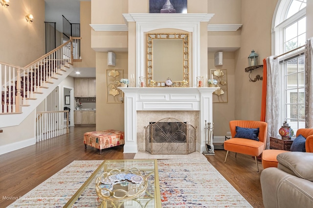 living room featuring wood finished floors, a towering ceiling, a tile fireplace, and stairway