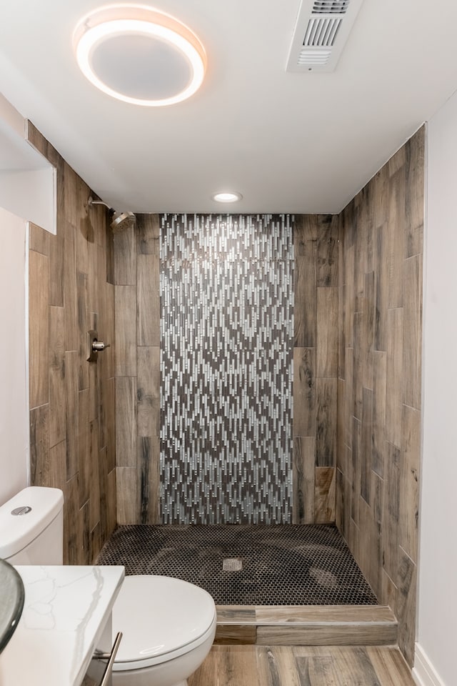 bathroom featuring tiled shower, vanity, wood-type flooring, and toilet