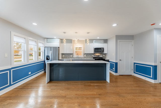 kitchen with pendant lighting, light hardwood / wood-style floors, white cabinetry, and stainless steel appliances