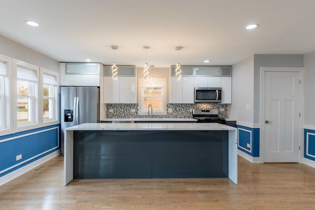 kitchen featuring hanging light fixtures, stainless steel appliances, a kitchen island, light hardwood / wood-style floors, and white cabinets