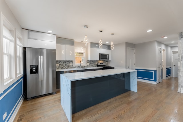 kitchen with light wood-type flooring, stainless steel appliances, a kitchen island, decorative light fixtures, and white cabinetry