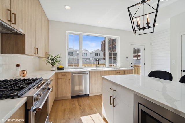 kitchen with light stone countertops, pendant lighting, light hardwood / wood-style floors, light brown cabinetry, and appliances with stainless steel finishes