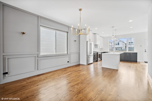 kitchen featuring light wood-type flooring, gray cabinetry, stainless steel appliances, pendant lighting, and white cabinetry