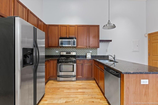 kitchen featuring pendant lighting, sink, light wood-type flooring, appliances with stainless steel finishes, and kitchen peninsula