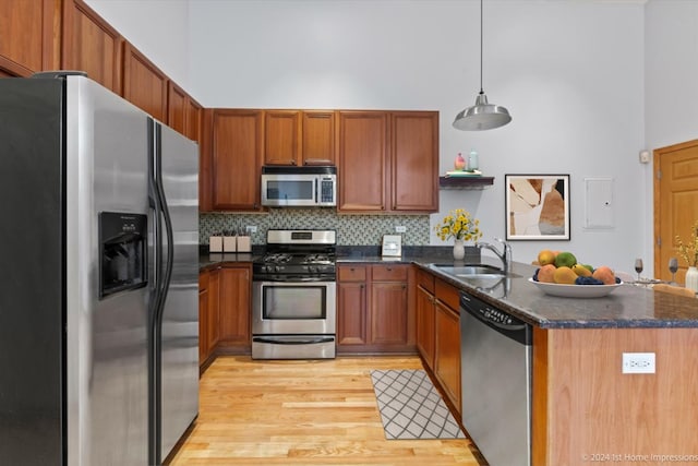 kitchen with decorative backsplash, appliances with stainless steel finishes, sink, decorative light fixtures, and light hardwood / wood-style floors