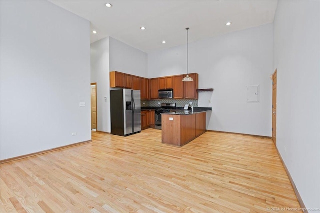 kitchen with pendant lighting, light wood-type flooring, a high ceiling, and appliances with stainless steel finishes