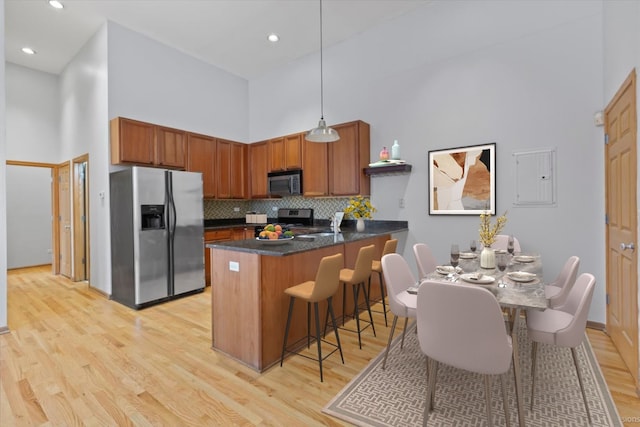 kitchen featuring a towering ceiling, hanging light fixtures, appliances with stainless steel finishes, and light hardwood / wood-style flooring