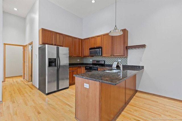 kitchen featuring light hardwood / wood-style flooring, kitchen peninsula, a towering ceiling, decorative light fixtures, and appliances with stainless steel finishes