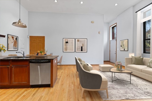 kitchen with pendant lighting, dishwasher, a high ceiling, sink, and light hardwood / wood-style flooring