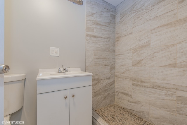 bathroom with a tile shower, vanity, and toilet