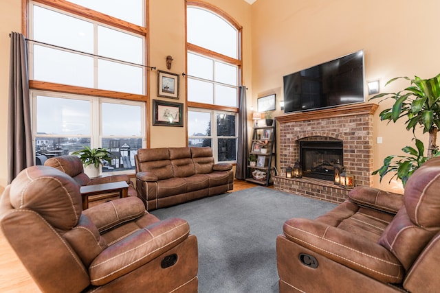 living room with hardwood / wood-style flooring, a towering ceiling, and a brick fireplace